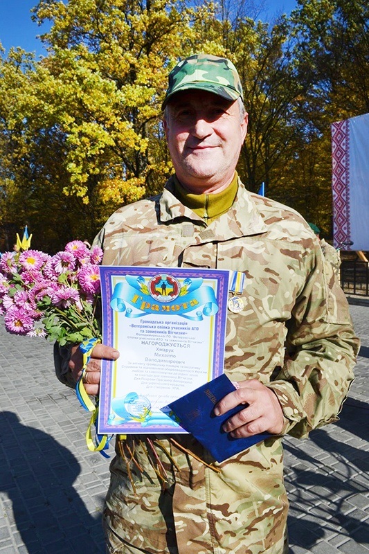 Михайло Хмарук з відзнакою та квітами. В букеті хризантем - стрічка та фенечка на руку в національних кольорах.